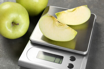 Kitchen scale with pieces of apple and fruits on grey textured table, closeup
