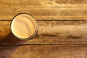 Glass of beer with froth on wooden table, top view. Space for text