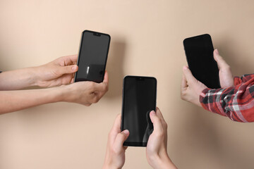 Women holding smartphones with blank screens against beige background, closeup. Mockup for design
