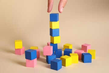 Obraz premium Woman putting colorful cube to other ones on beige background, closeup