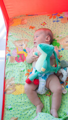 Baby with toy lies down in bed. About 7 months.