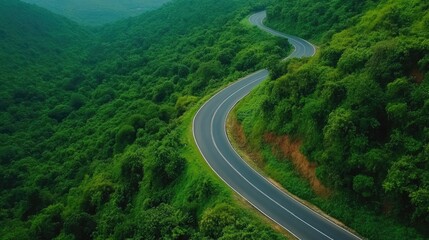 Aerial view of an asphalt road curving through green forest and mountain landscape.