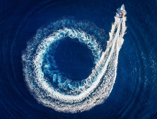 Aerial top view of a motor RIB boat forming a circle of waves and bubbles with its engine over the blue sea
