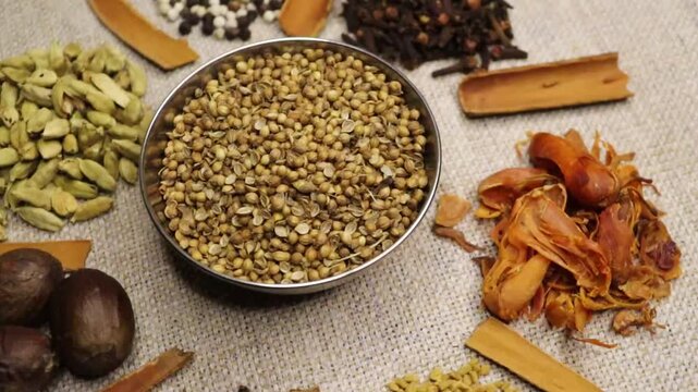Cilantro coriander seeds spinning clockwise slowly top down view. 4k video. Mixed whole Indian spices in background. 