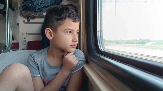 A 10-year-old boy travels on a train and looks out the window