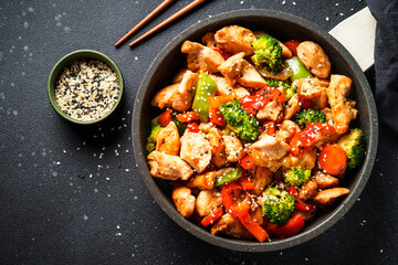 Chicken stir fry with vegetables and sesame at black background. Traditional asian cuisine.