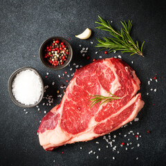 Raw meat steak with spices on black background. Beef steak ribeye. Top view with copy space.