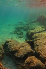 Shallow sea, big rock with sunrays. Seabed with the marine life, underwater photography from early morning snorkeling. Wildlife in the ocean and sun. Undersea landscape, adventure snorkeling.