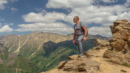 Fototapeta premium A man looks at the high snow-capped mountains. The conquest of the mountains. The rocks are located high in the mountains. The nature of the highlands.