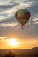colorful hot air balloon flying in the air piloted by people under cloudy skies at sunset