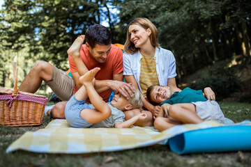 Family of four making beautiful memories while camping in the forest. The children are lying on the...