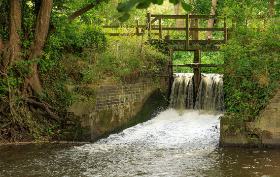 Water pouring over the sluce gates of  a wooden weir