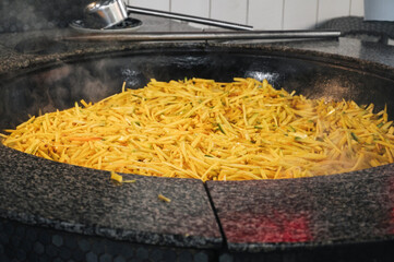 yellow carrots are stewed in a cauldron for cooking traditional Asian Uzbek pilaf in the kitchen at...
