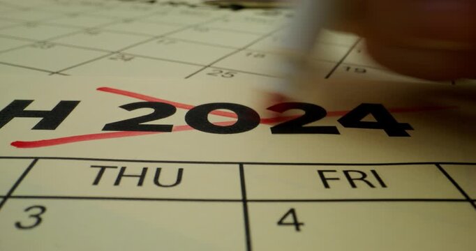 A person crosses out the year in the schedule table with a red marker. Close-up of the marker, an unrecognizable person