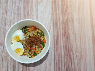 A bowl of fried noodles with various toppings on a wooden table. Soft focus. Semi flat lay. 