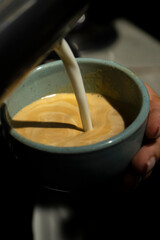Milk is poured into a cup of freshly brewed coffee. The process of preparing cappuccino, latte. Close-up. Vertical photo. High quality photo