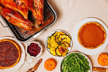 A beautifully arranged Thanksgiving meal with a golden roast turkey in a pan and traditional dishes. Pumpkin and pecan pies, green beans and roasted vegetables.