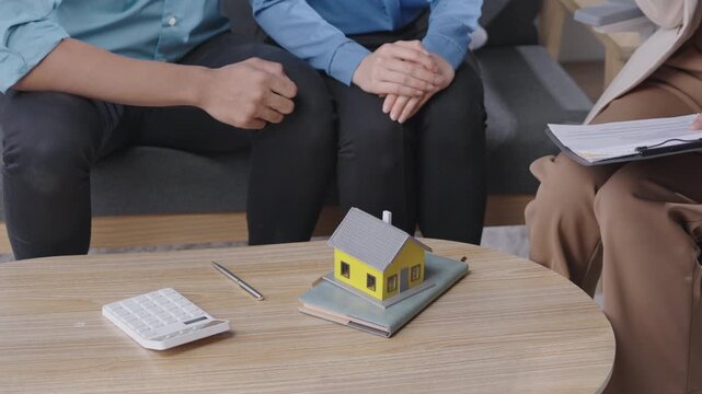Professional real estate agent consulting a couple with a house model, notebook, pen, and calculator during a property discussion. Ideal for real estate services and homebuying process visuals