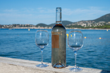 Tasting of cold rose wine from Provence outdoor on wooden yacht pier with view on blue water and white sandy beach Plage de Pampelonne near Saint-Tropez, summer vacation in France