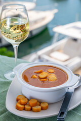 Homemade tasty fish or bisque soup with croutons served with glass of cold white wine and view on yacht boats and houses of Port Grimaud, French Riviera, France. Food of Provence