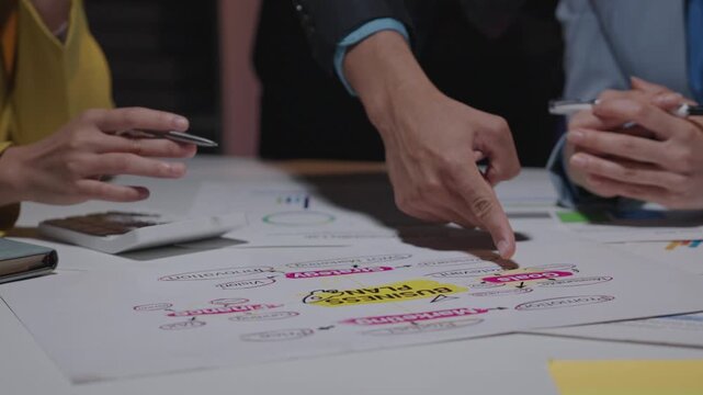 Team members collaborate in a brainstorming session, planning creative ideas. Hands point at a colorful mind map on a white sheet