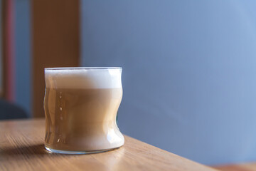 Close-up side view of drinking glass with latte macchiato standing on wooden table in cafe or restaurant. Copy space. Soft focus. Coffee beverages theme.
