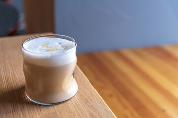 Close-up side view of drinking glass with latte macchiato standing on wooden table in cafe or restaurant. Copy space. Soft focus. Coffee beverages theme.