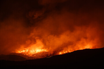 Fototapeta premium Reflections of a massive wildfire blaze in the night over the hills