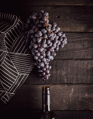 a bunch of grapes and neck of a wine bottle on a black wooden background with rag napkin