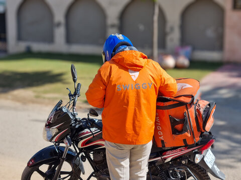 Rider delivery boy from food and hyperlocal delivery app Swiggy standing and checking for orders with his bike