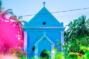 Little blue church surrounded by palm trees and beautiful flowers.