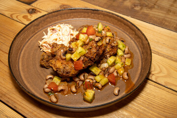 A delicious plate of home made fried chicken with beans and cut vegetables on a wooden kitchen table