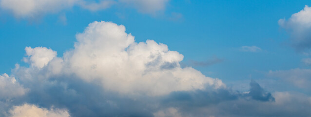 Obraz premium White curly clouds in the blue sky, slightly illuminated by the evening sun