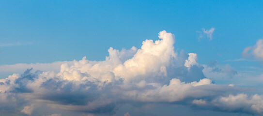 White curly clouds in the blue sky, slightly illuminated by the evening sun