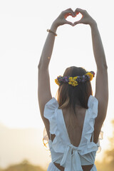 A woman raises her hand above her head to make a heart symbol on the background of the bright...