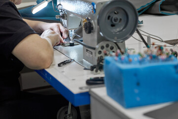 A woman dressmaker on an automatic sewing machine makes a neat stitch, sews details. In a garment factory, the working process of sewing a fabric product