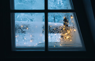 Looking out the frosty winter window. Christmas lights and snow on background. Cozy holiday concept.