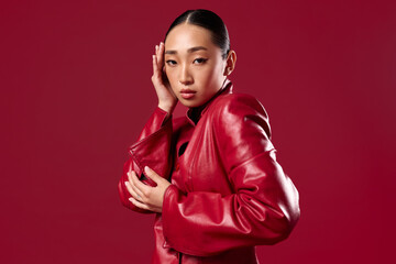 Asian woman in red leather jacket posing for camera on red background stunning beauty and fashion