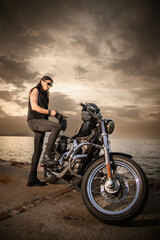 Fototapeta premium Man with Chopper Motorcycle by the Sea at Sunset..