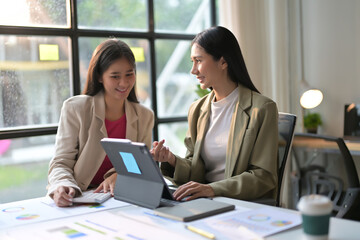 Two Businesswomen Collaborating on a Project in a Modern Office with Laptops and Documents