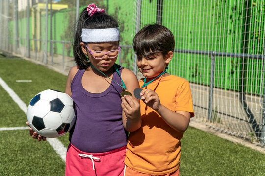 Young boy and girl with medals and soccer ball on field