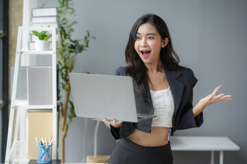Asian businesswoman is looking surprised while holding a laptop in an office setting