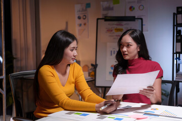 Two businesswomen working late in office having business discussion about financial report