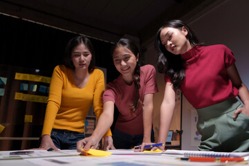 Three female marketing professionals working late in the office, collaborating on a project using sticky notes and brainstorming ideas
