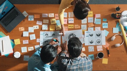 Top down aerial view of skilled designer hold logo while discuss with team. Aerial business group...