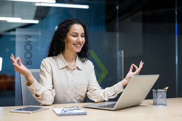 Businesswoman practicing meditation at office desk looking happy and relaxed. Creating balance at work, promoting mental health and stress relief. Modern office environment.