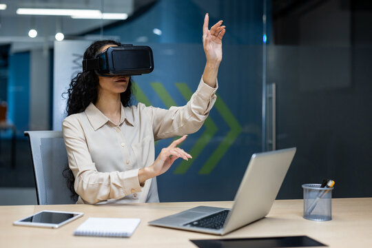 Businesswoman using virtual reality headset in modern office, interacting with digital interface. Young woman immersed in VR technology, exploring virtual workspace, innovation in business