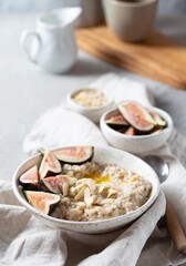 A wholesome bowl of oatmeal topped with fresh figs and sliced almonds, set on a rustic linen cloth. Accompanying small bowls of figs and almonds enhance the cozy breakfast scene