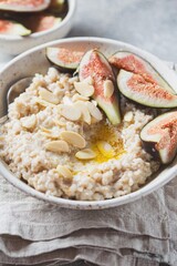 A wholesome bowl of oatmeal topped with fresh figs and sliced almonds, set on a rustic linen cloth. Accompanying small bowls of figs and almonds enhance the cozy breakfast scene