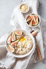A wholesome bowl of oatmeal topped with fresh figs and sliced almonds, set on a rustic linen cloth. Accompanying small bowls of figs and almonds enhance the cozy breakfast scene